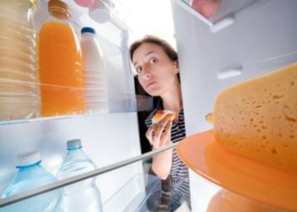 donna che apre un frigorifero mentre tiene in mano un tortino