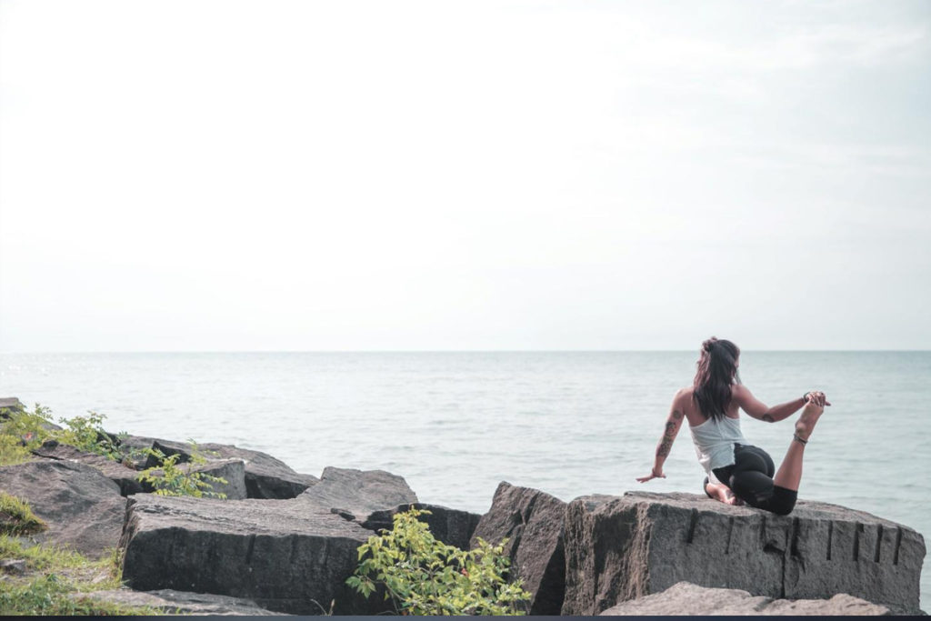 Donna pratica yoga all’alba sul mare approfittando dei benefici che questo connubio offre