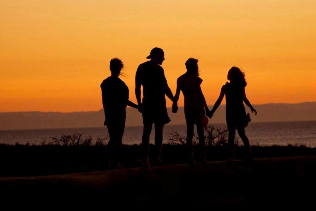 Membri di una famiglia per mano davanti al tramonto.