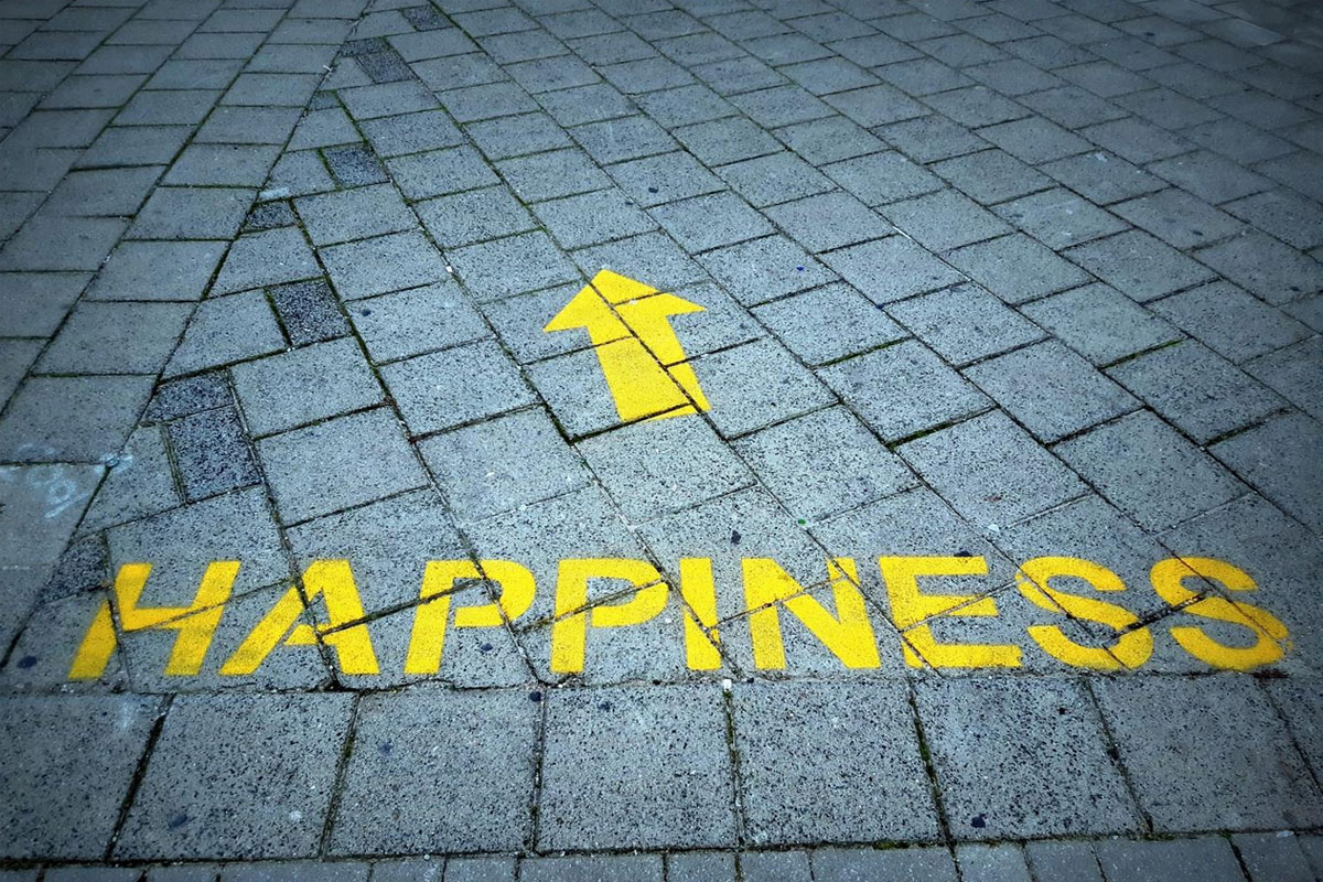 Scritta “Happiness” con freccia su strada.