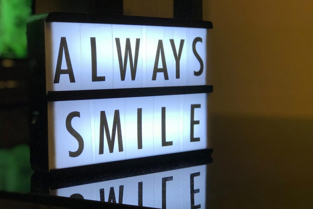 Scritta luminosa “Always Smile” su piano riflettente.