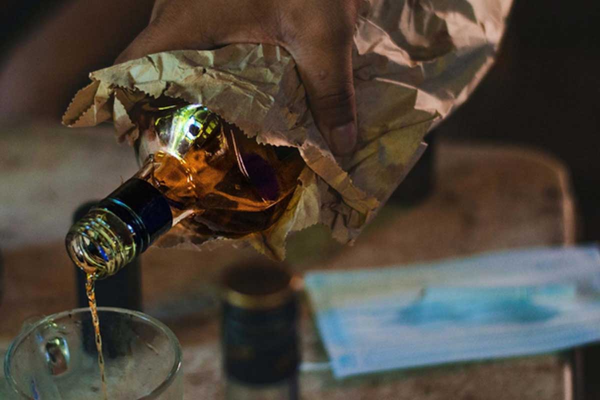 Alcolico contenuto in una bottiglia di vetro, nascosta in una busta di carta e il cui contenuto è versato in un bicchiere