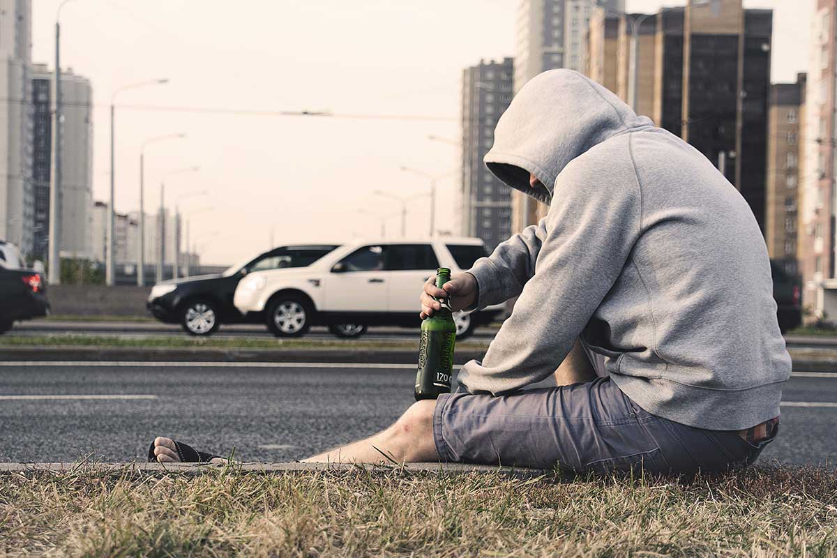 Uomo vestito in maniera sportiva, che beve una birra in mezzo alla strada