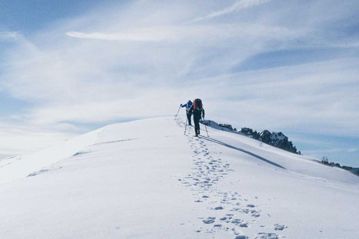 Due persone con uno zaino sulle spalle che scalano la cima di una montagna completamente innevata