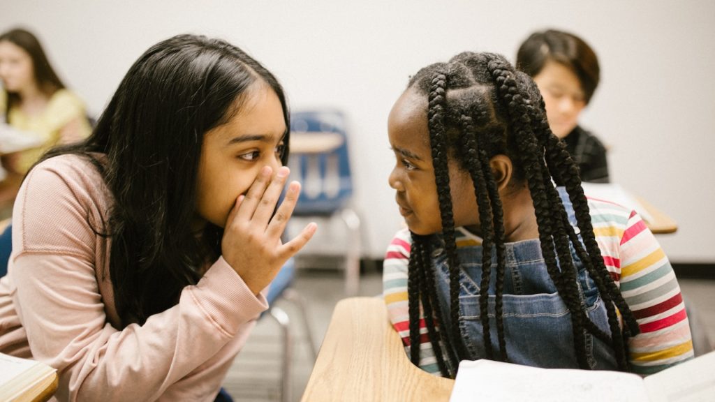 Due bambine chiacchierano tra loro in classe, durante una lezione. Il disturbo oppositivo provocatorio porta a sfidare apertamente l'autorità degli adulti.