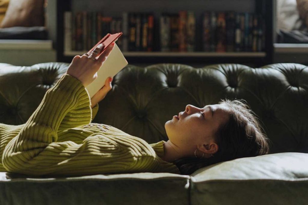 Donna rilassata che legge libro stesa sul divano