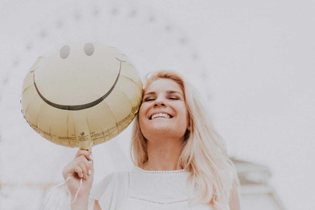 Donna con atteggiamento positivo che sorride con palloncino in mano a forma di smile