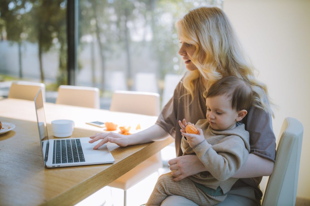 una giovane madre lavora al pc mentre tiene in braccio il bimbo