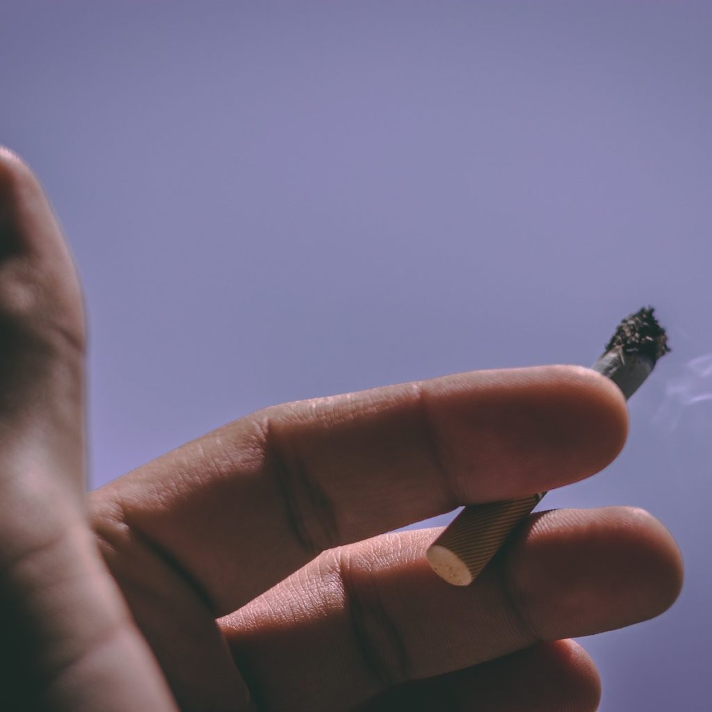 Tabagismo: un fumatore stringe tra indice e medio una sigaretta accesa