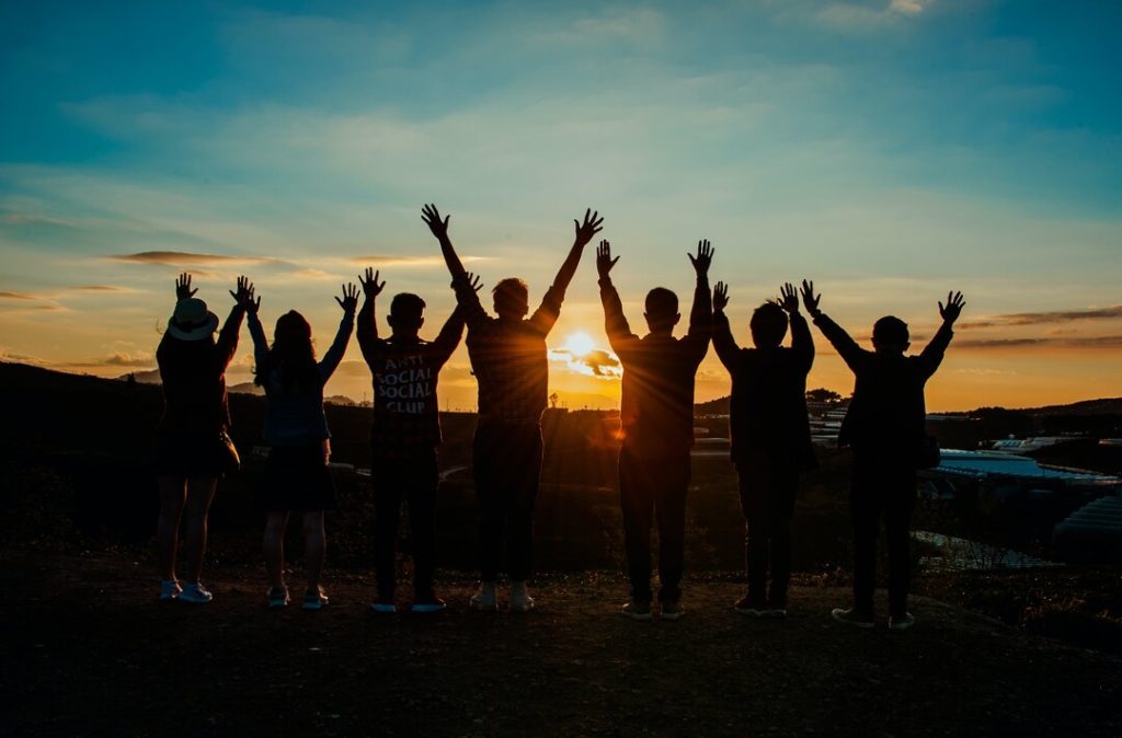 gruppo di persone con le mani al cielo guarda il tramonto