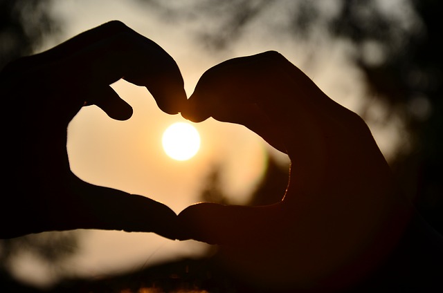 due mani che formano un cuore con il sole che tramonta al centro