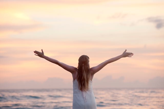 una ragazza guarda il mare con le braccia aperte in segno di benessere
