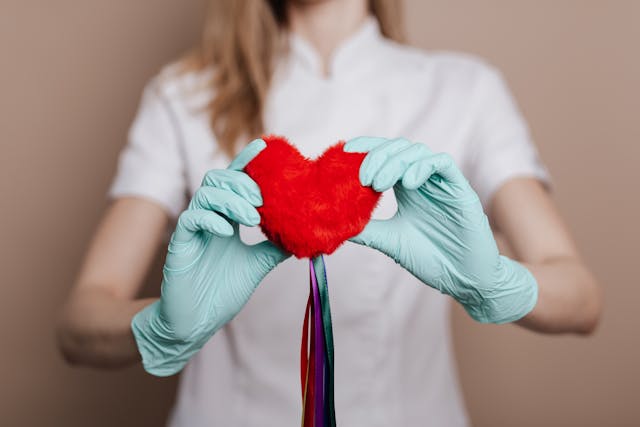 mani con guanti chirurgici tengono in mano un cuore di peluche