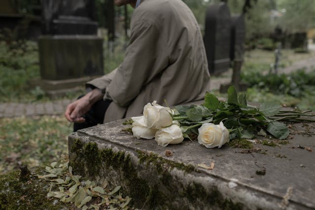 uomo seduto in un cimitero con rose bianche