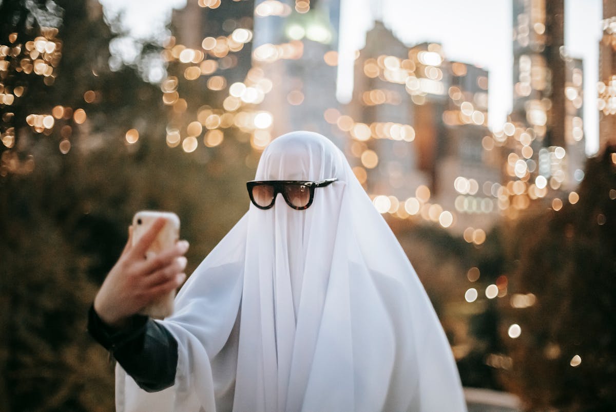 Ghosting: un ragazzo vestito da fantasma con lo smartphone in mano