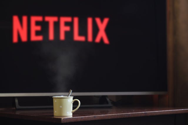 schermo televisivo con scritta rossa netflix e una tazza di te sulla mensola